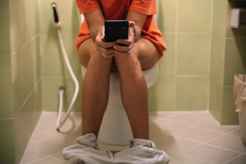 Una mujer sentada en el inodoro con un celular en la mano.