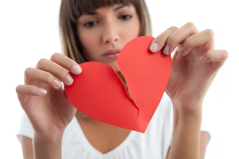Foto de mujer rompiendo corazón de papel.