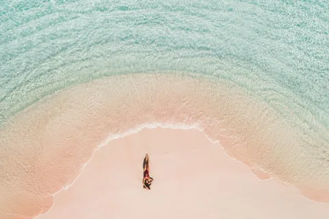 Una mujer tomando sol en una playa de arena rosa