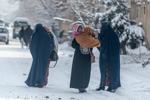 Mujeres afganas vestidas con burka llevan niños mientras caminan por una calle nevada en Kabul .