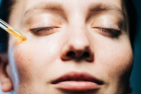 una mujer con un gotero aplicandose un serum en el rostro