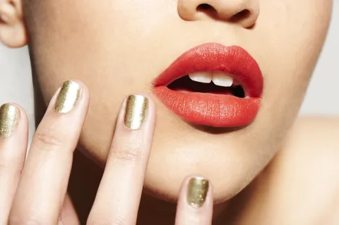 Una mujer con los labios en color rojo y las uñas doradas