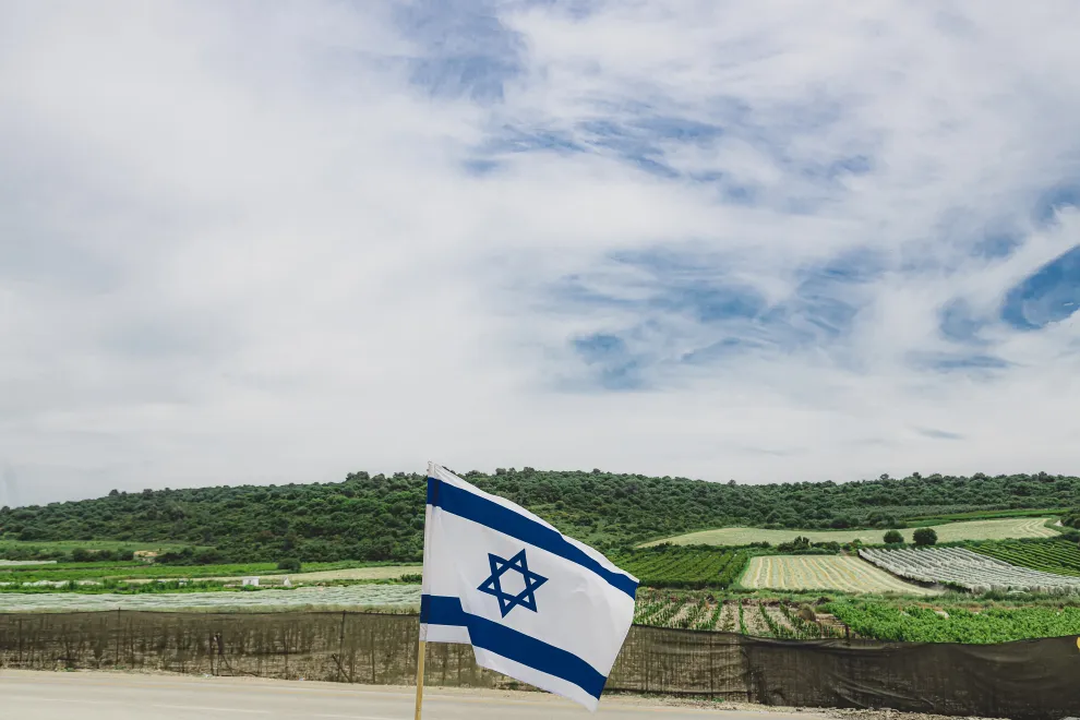 Bandera nacional israelí ondeando contra los campos agrícolas del Kibbutz en el norte de Israel.